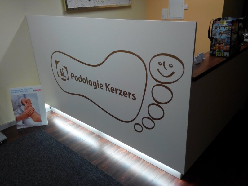Empfangstheke der Podologie Kerzers mit grossem Fuss-Signet und dem Schriftzug «Podologie Kerzers»